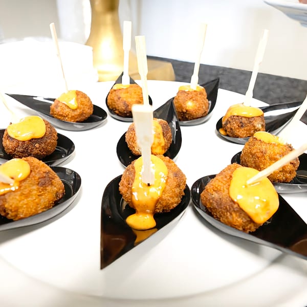 Crispy fried croquettes with yellow sauce, each on a black spoon with a toothpick.