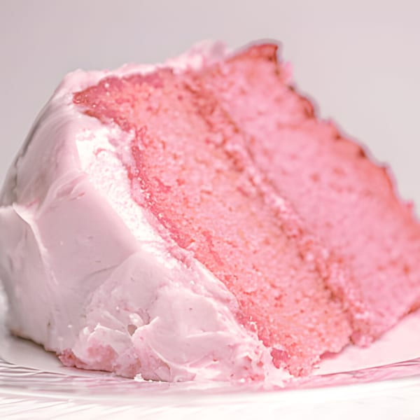 A close-up of a slice of pink cake with pink frosting on a white plate.