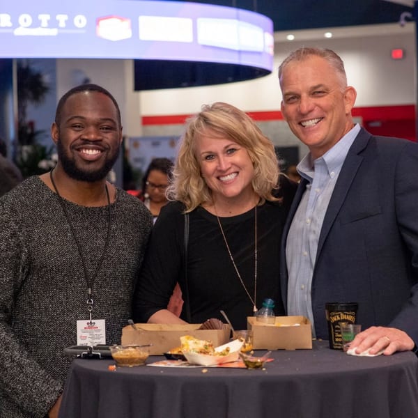 Three smiling guests enjoying food and drinks at a Grotto event.