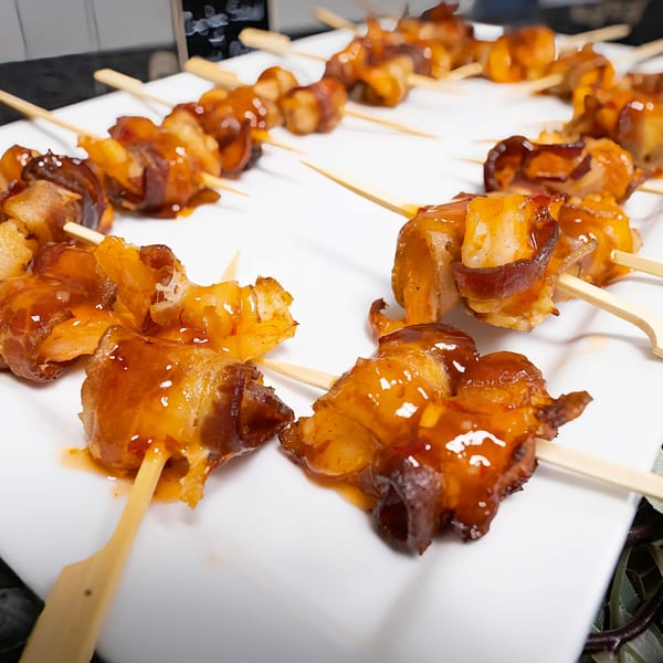 Sweet and savory glazed bacon-wrapped skewers on a white platter.