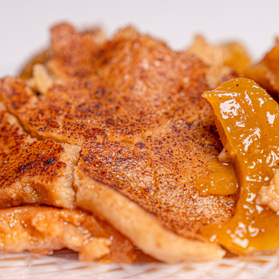 Close-up of a golden, flaky pastry layered with crisp browned sheets and glossy orange glaze.