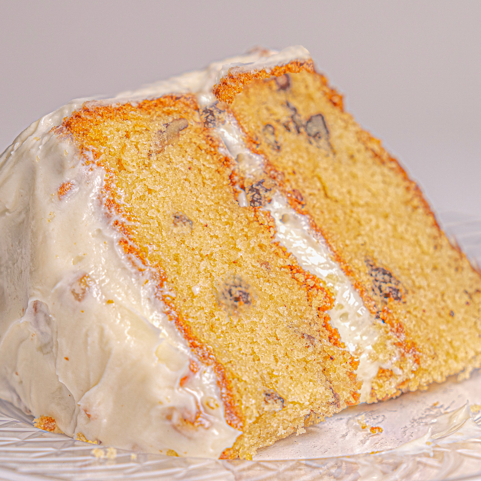 Close-up of a golden layered cake with creamy frosting and dark chocolate pieces on a glass plate.