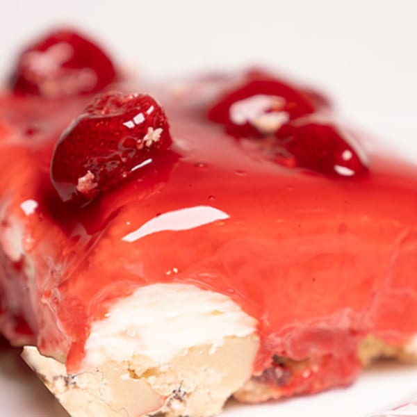 Close-up of a Mikki's Soul Food Cafe strawberry cheesecake slice with red glaze and fresh strawberries.