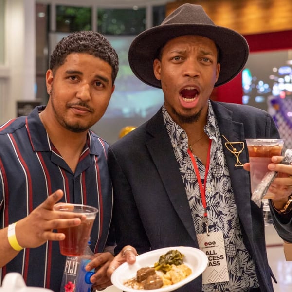 Two men enjoying drinks and food at a restaurant event, one looking surprised.