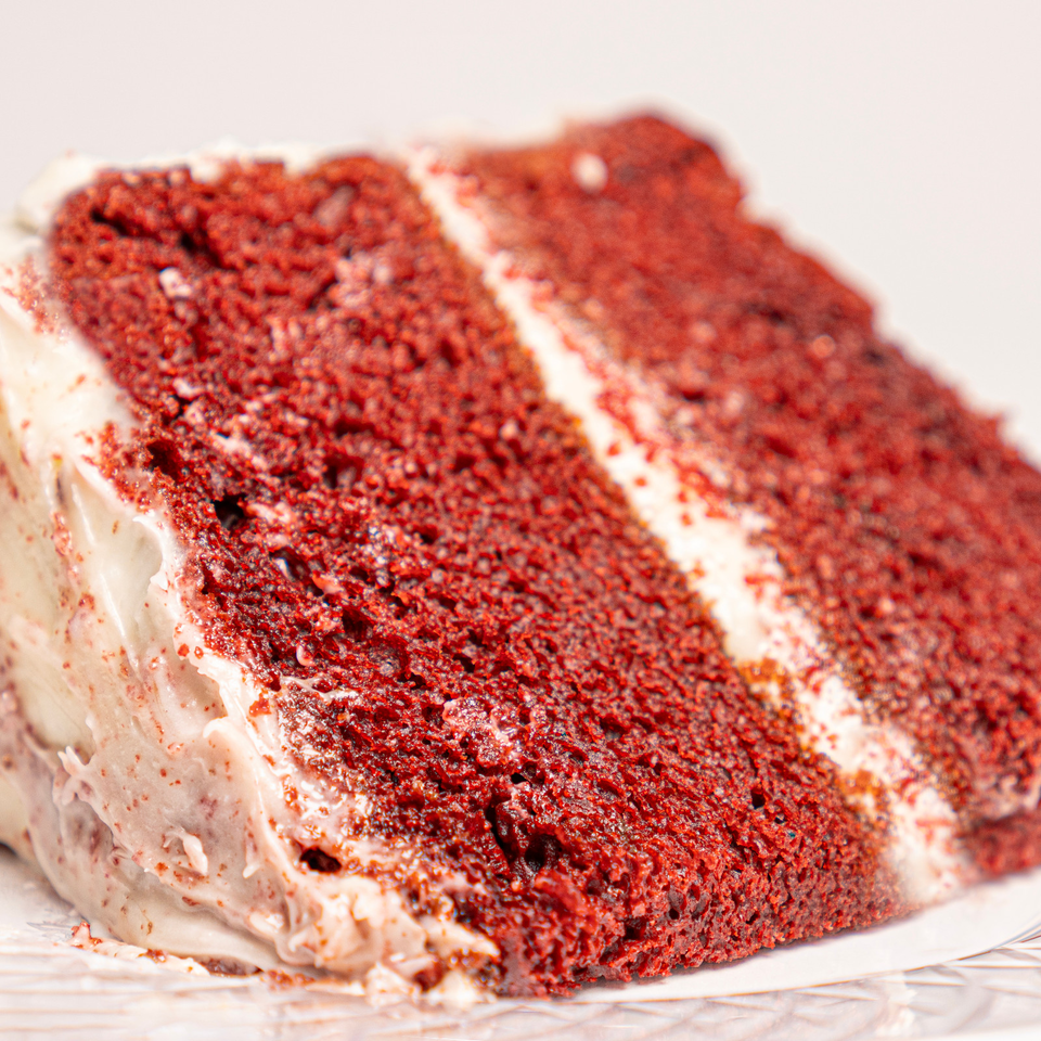 Close-up of a chocolate cake covered with red crumbs and layered with creamy frosting on a plate.